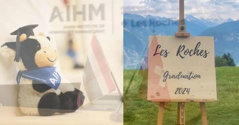 ตุ๊กตาวัวนุ่มนิ่มสวมหมวกและผ้าพันคอรับปริญญาอยู่ข้างธงเล็กๆ ที่มีคำว่า "AIHM" อยู่ด้านหลัง ทางด้านขวามีป้ายไม้เขียนว่า "Les Roches Graduation 2024" โดยมีฉากหลังเป็นทิวทัศน์ภูเขาที่สวยงาม