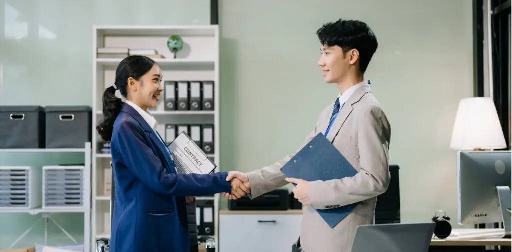 Two business professionals shaking hands in an office setting during a leadership training session for middle-level management development at AIHM.