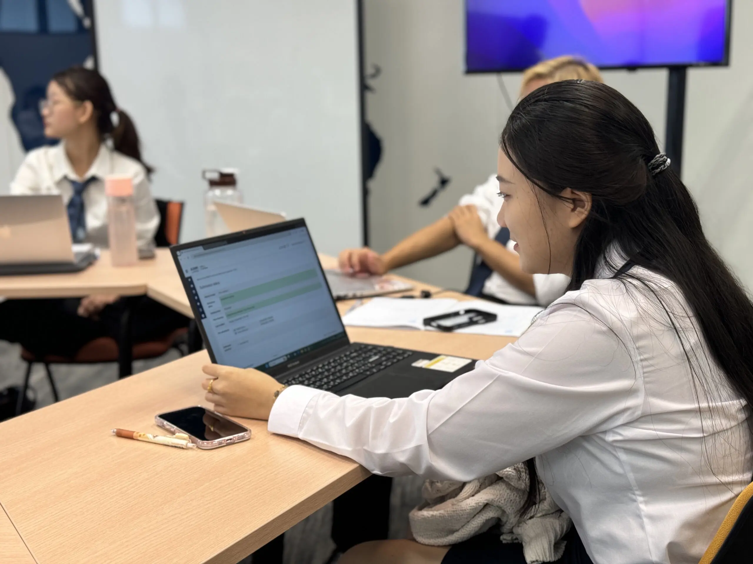 AIHM hospitality management student using a laptop during an English for Business and Academic Study session, building academic writing and research skills in a modern classroom.