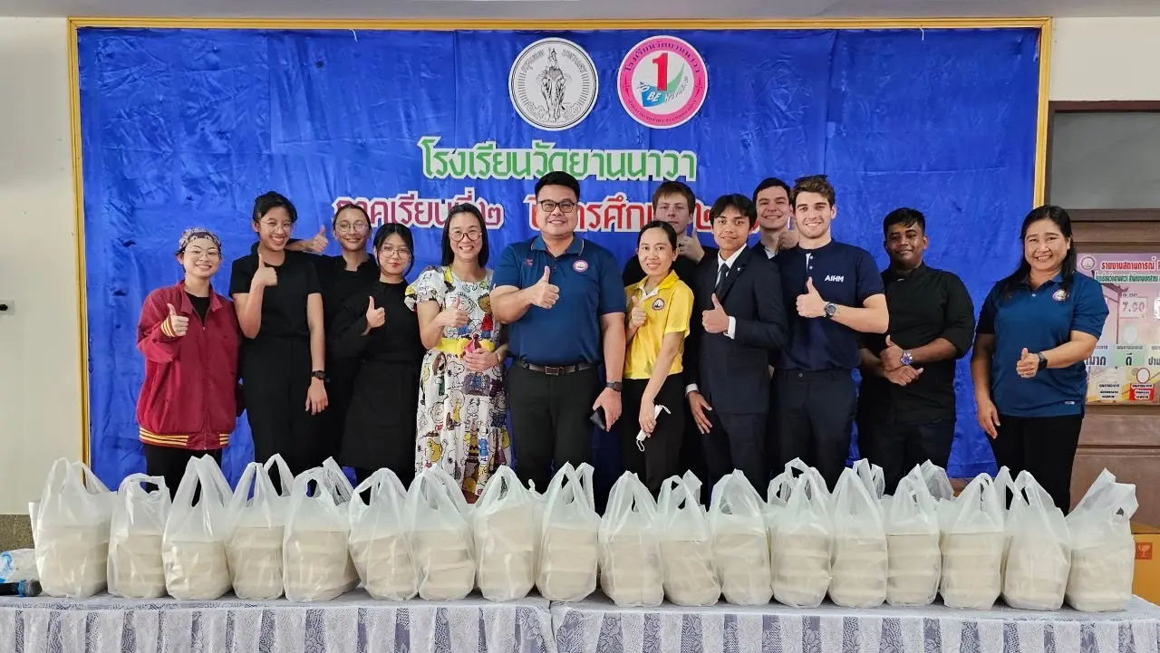 AIHM hospitality students and community partners delivering meal donation packs during a CSR outreach event at a local Thai school, promoting community service and youth engagement.