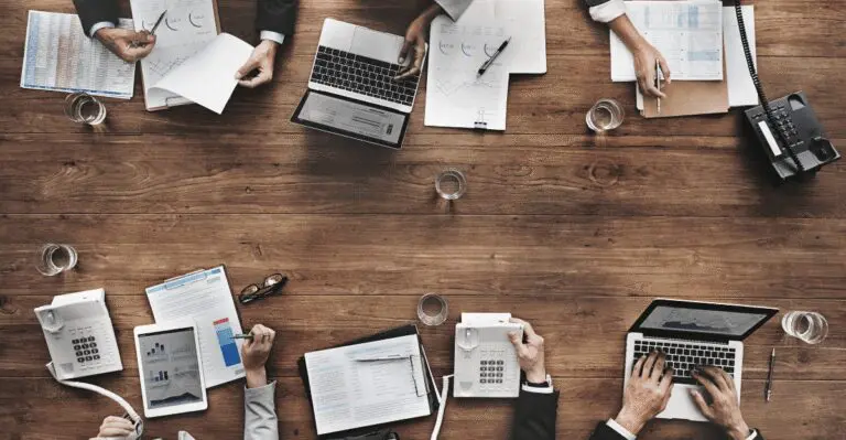 Overhead view of a business team working with laptops, reports, and phones, illustrating teamwork and operations for an AIHM article
