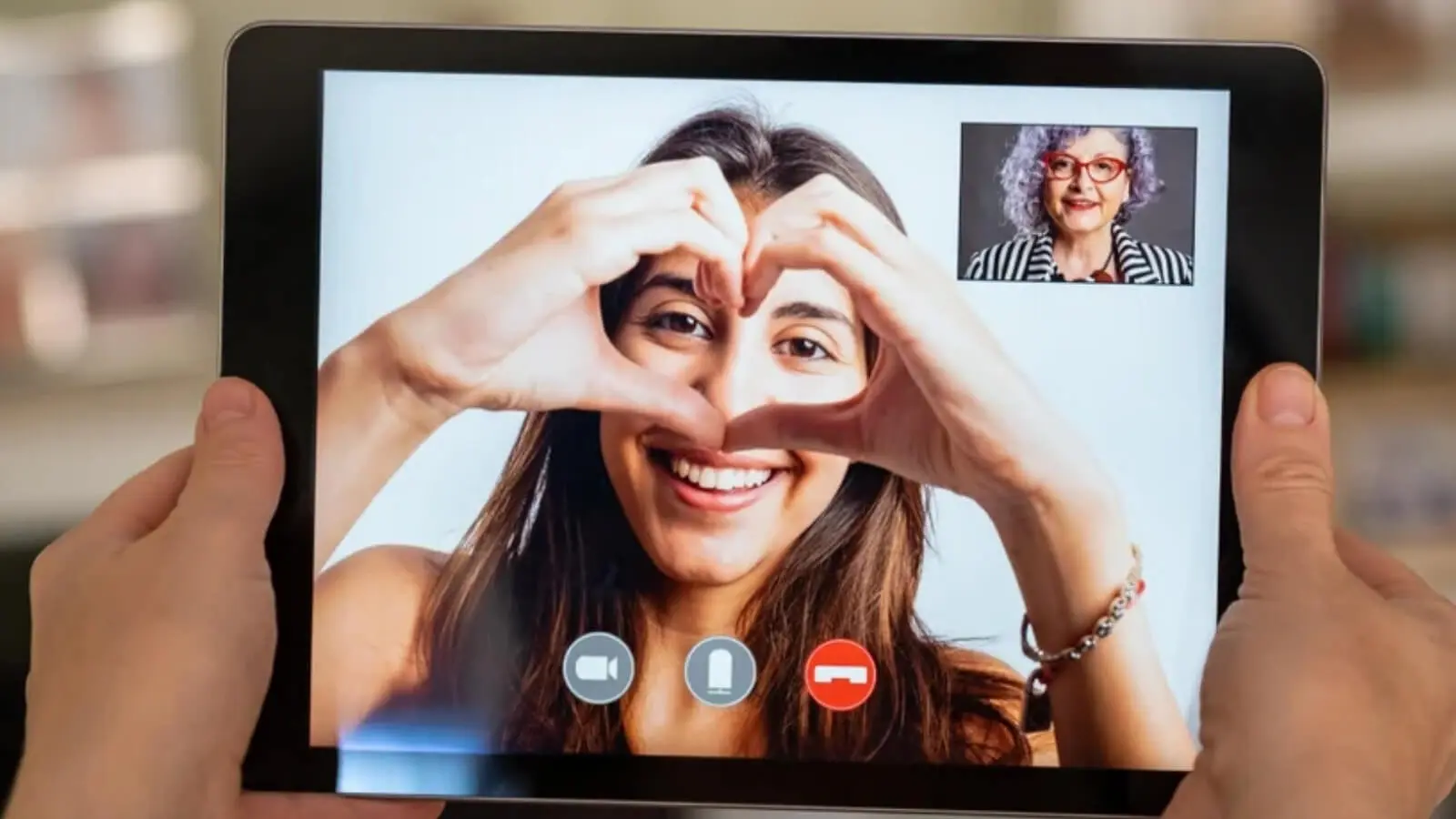 Young woman making heart shape with hands during video call on tablet, smiling warmly at screen, staying connected with family while studying abroad, international student communication