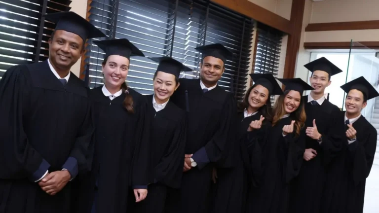Diverse AIHM graduates smiling together in academic gowns after completing the Hotel Management Certificate programme in Bangkok