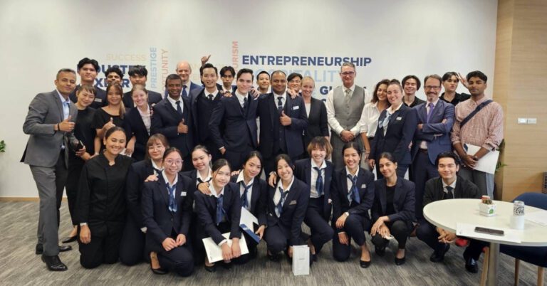 A diverse group of 30 people, mostly in business attire, smile and pose in a well-lit room with "Entrepreneurship" on the wall. The mood is celebratory and professional.