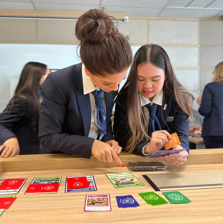AIHM students examine game cards during hospitality Monopoly classroom activity, Bangkok