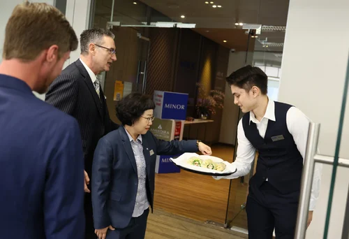 A server in a vest offers appetizers on a tray to professionals in suits, conveying a formal and hospitable atmosphere in an office lobby.