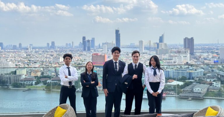 A group of five people in formal attire standing on a rooftop with a city skyline in the background. They appear confident and professional.
