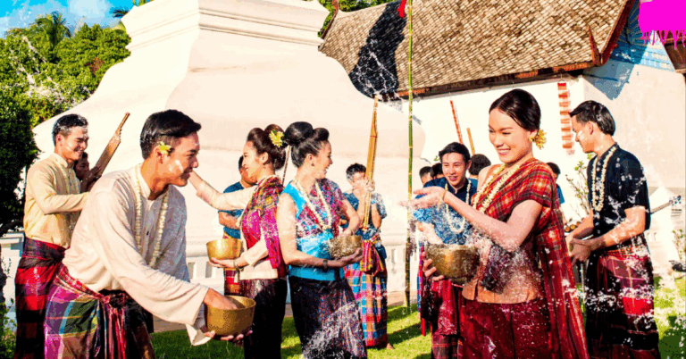 A group of people wearing colorful traditional clothing joyfully splash water at each other outdoors, conveying a festive and lively atmosphere.
