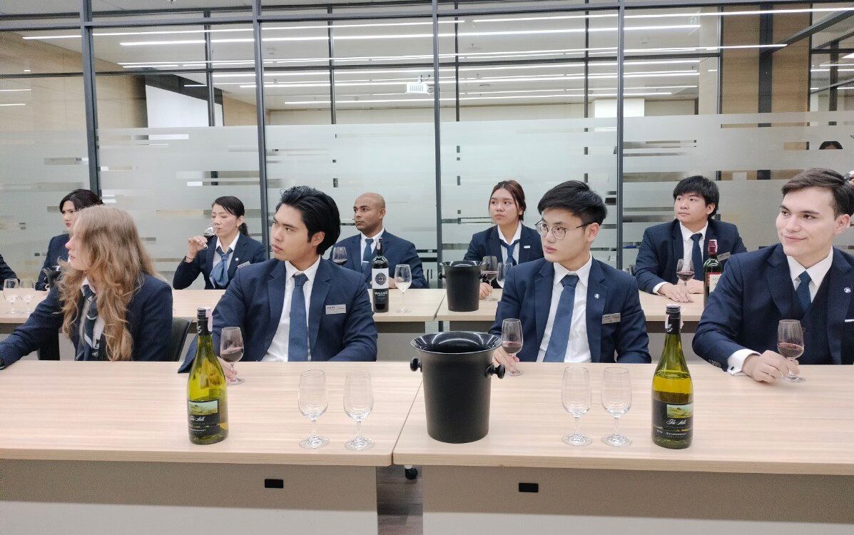 AIHM hospitality management students in uniform participating in a wine appreciation and service training class, gaining practical skills as part of their BBA hospitality curriculum in Bangkok.