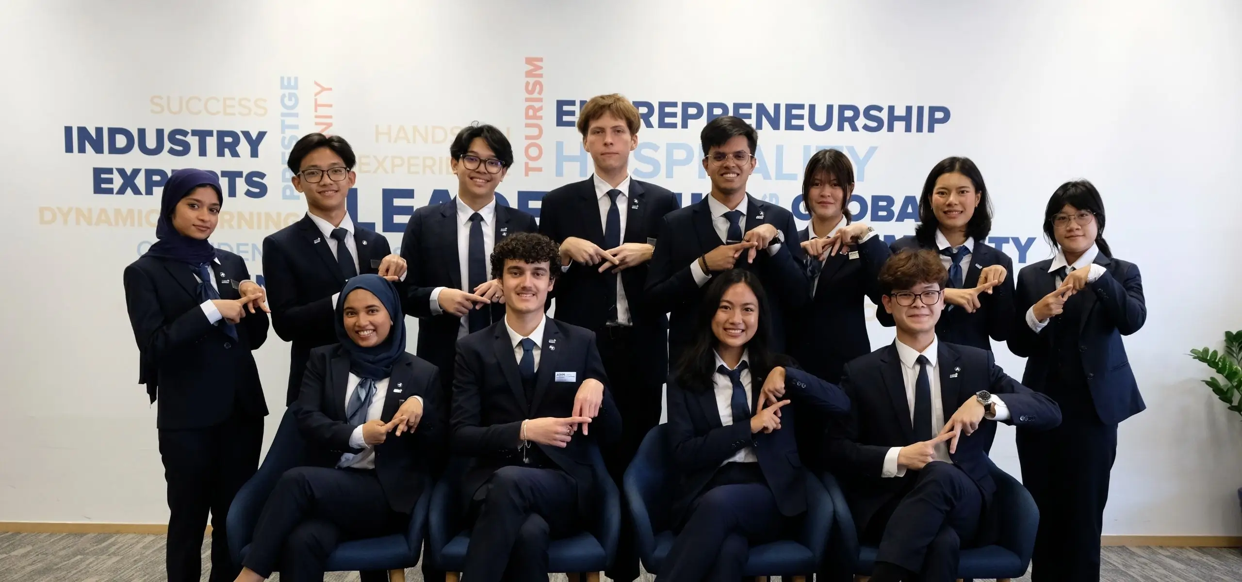 AIHM student committee in formal business attire in front of a wall featuring words like leadership, entrepreneurship, and hospitality