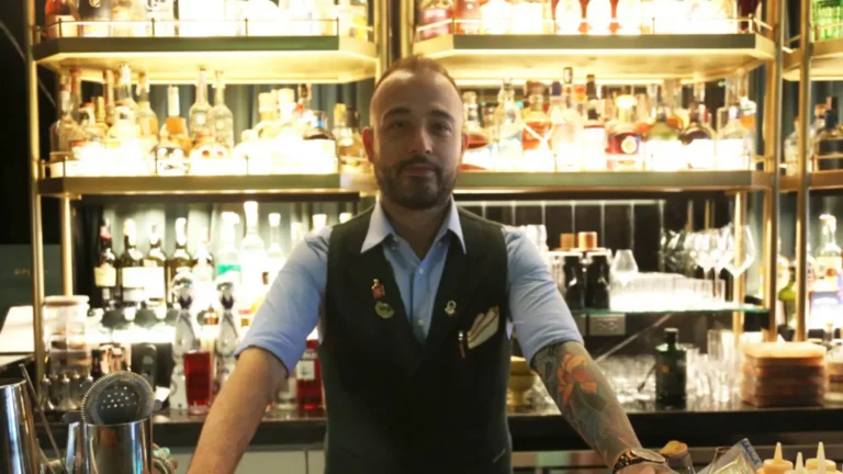 Matteo Cadeddu, Opium Bar's head mixologist and bar manager poses behind bar shelves for AIHM blog feature, The Inside Scoop